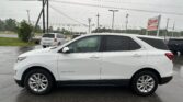 White Chevrolet Equinox parked in a wet parking lot with power lines and a sign in the background on a rainy day.