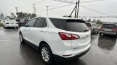 White Chevrolet Equinox in the foreground of a rainy car dealership lot, with many cars, wet pavement, and overhead power lines.