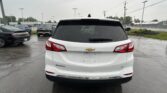 Rear view of a white Chevrolet Equinox LT in a wet parking lot, other cars and power lines in the background.