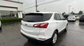 White Chevrolet SUV parked in a wet parking lot beside a white building with red trim.