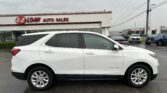 White Chevrolet Equinox in the foreground at a car dealership, with an E-Z Loan Auto Sales building and red sign in the background under a cloudy sky.