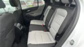 Rear passenger seats of a modern car with quilted gray upholstery and black trim, visible headrests and seat belts, rain on the side window outside the car door.