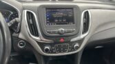 Interior of a car showing the center touchscreen, climate controls, and gear lever, with a rainy car lot outside.