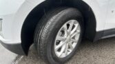 Close-up of a light-gray car wheel and tire on a wet road, with rain droplets on the fender and a Chevrolet center cap visible on the rim.