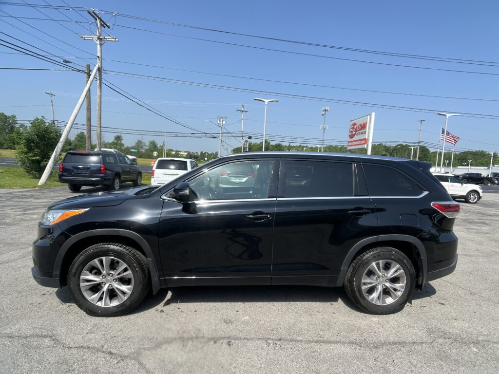 Close-up of a black SUV in a parking lot with utility poles and power lines, dealership sign and an American flag in the distance.