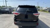 Rear view of a black Highlander SUV parked in a lot with other cars and overhead power lines in clear weather.