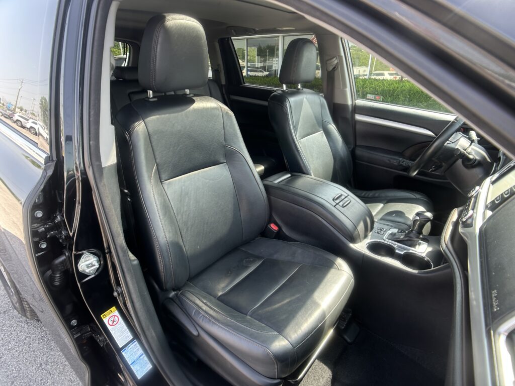 Front interior of a black leather-car showing driver and front passenger seats with center console and cup holders; door open.