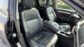 Front interior of a black leather-car showing driver and front passenger seats with center console and cup holders; door open.