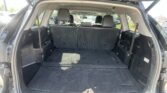 Open SUV tailgate revealing a spacious black cargo area with third-row seats upright and dark carpeting inside.