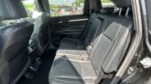 Rear interior of a black leather SUV with two row of seats, headrests, and door panel visible; outside cars seen through windows