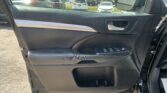 Driver-side car door interior panel with window controls and chrome handle; view of parking lot with multiple cars through the open window and side mirror outside