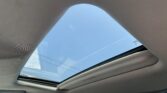 Open sunroof in a car exposing bright blue sky through the opening above beige headliner, no people visible.