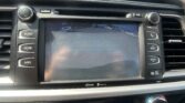 Center console of a car showing a touchscreen navigation/rear-view camera display with blue guide lines, flanked by physical audio controls and climate dials.