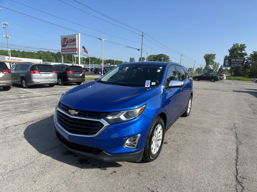 Blue Chevrolet SUV in the foreground at a car dealership lot with other vehicles and a tall EZ Loan Auto sign in the background.