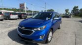 Blue Chevrolet SUV in the foreground at a car dealership lot with other vehicles and a tall EZ Loan Auto sign in the background.