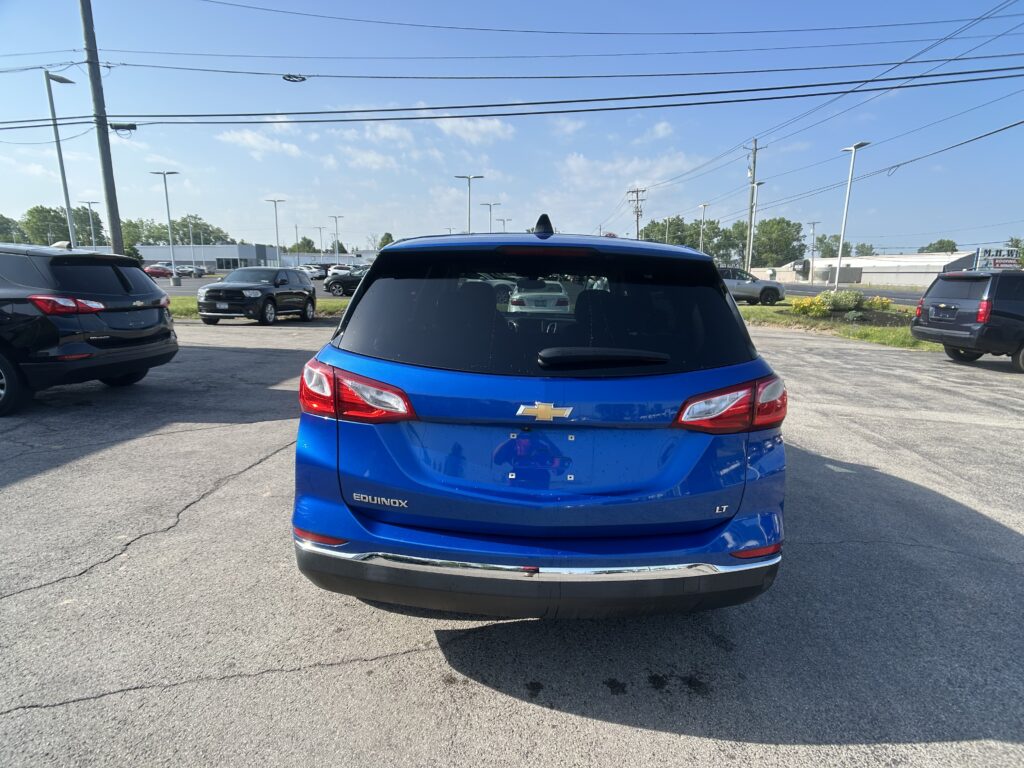 Rear view of a blue Chevrolet Equinox LT in a parking lot, with other cars and overhead power lines against a clear sky.