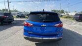 Rear view of a blue Chevrolet Equinox LT in a parking lot, with other cars and overhead power lines against a clear sky.