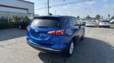 Blue Chevrolet SUV in a car dealership lot with a Toyota showroom and row of cars under a clear blue sky.