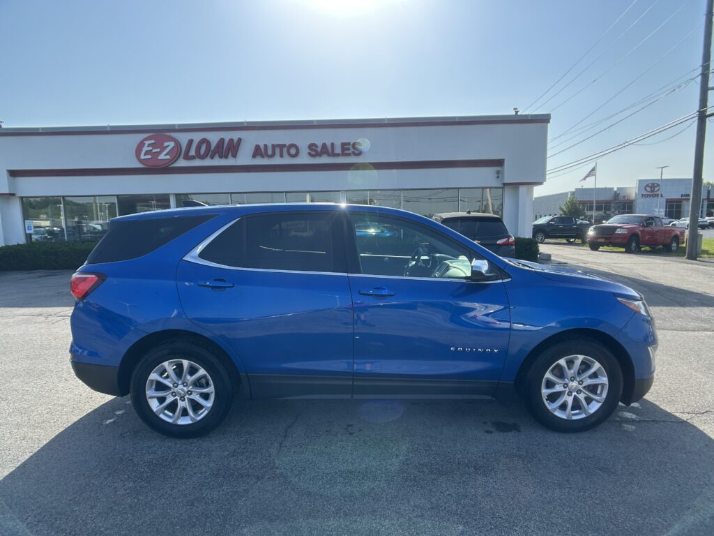 Blue Chevrolet Equinox SUV parked in front of the E-Z Loan Auto Sales storefront in a car dealership lot, with other vehicles visible in the background.
