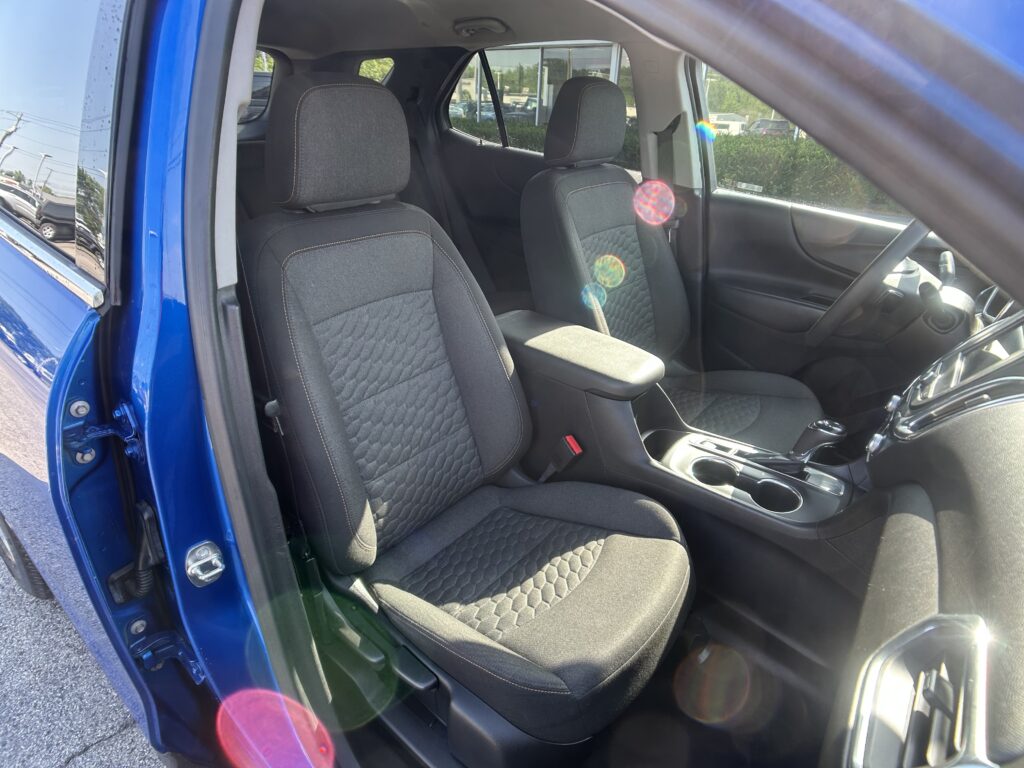 Blue car door open to reveal the front seat area with two black fabric seats and center console.