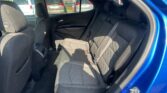 Rear seating area of a blue car with black cloth seats, headrests, and visible seat belts; parking lot outside through windows.