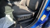 Front interior of a blue car showing the driver’s seat area, center console with gear shifter, and armrest, all in black fabric upholstery and daylight shadows.