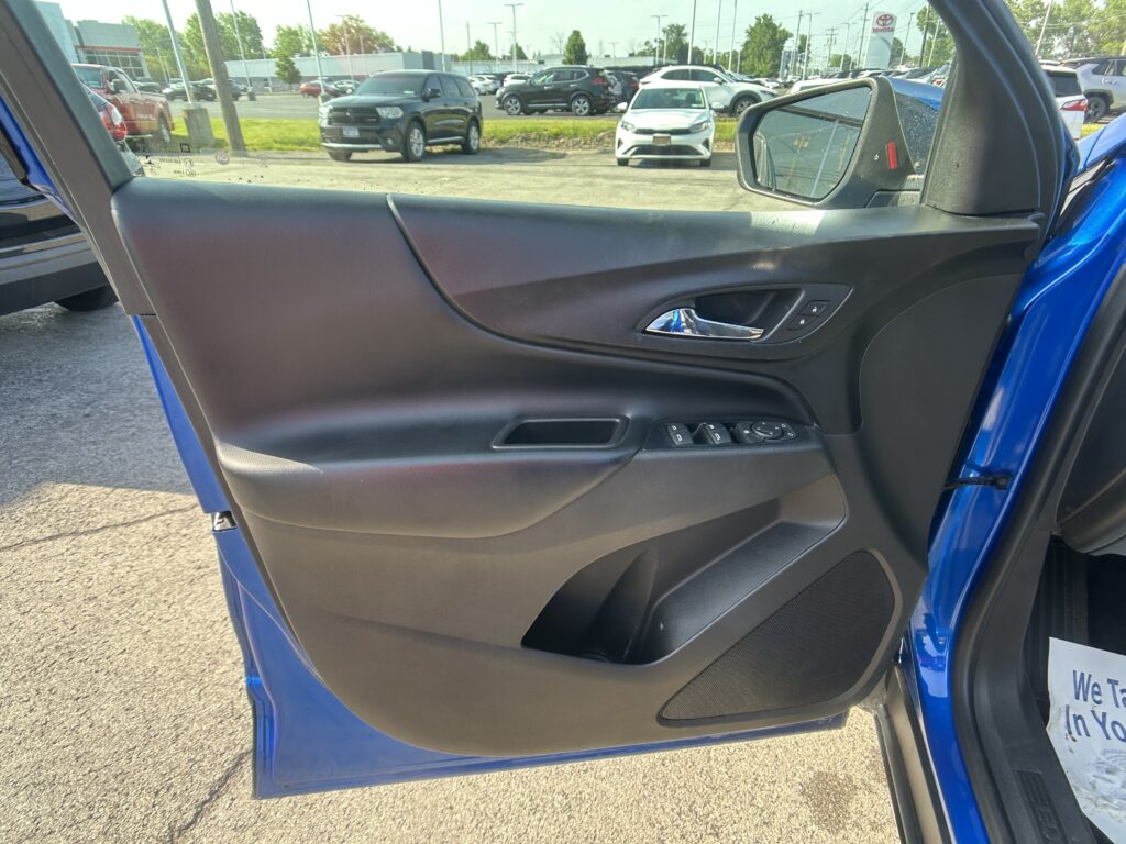 Interior of a car door with window controls visible; outside a parking lot with several vehicles and a side mirror in view