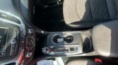 Front interior of a car: center console with climate controls, gear shifter, cup holder with keys, and parts of the driver seat.