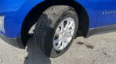 Close-up of a blue SUV wheel and tire, showing the front fender and wheel well area on a sunny day.