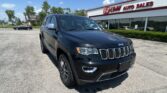 Black Jeep SUV parked diagonally in a lot outside an EZ Auto Sales dealership, with a blue sky and trees in the background.