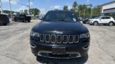 Front view of a black Jeep SUV in a car dealership lot with other vehicles and a building in the background.