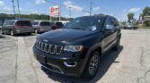 Close-up of a black Jeep SUV in a dealership parking lot with several minivans and an E-Z LOAN Auto Sales sign in the background on a sunny day.