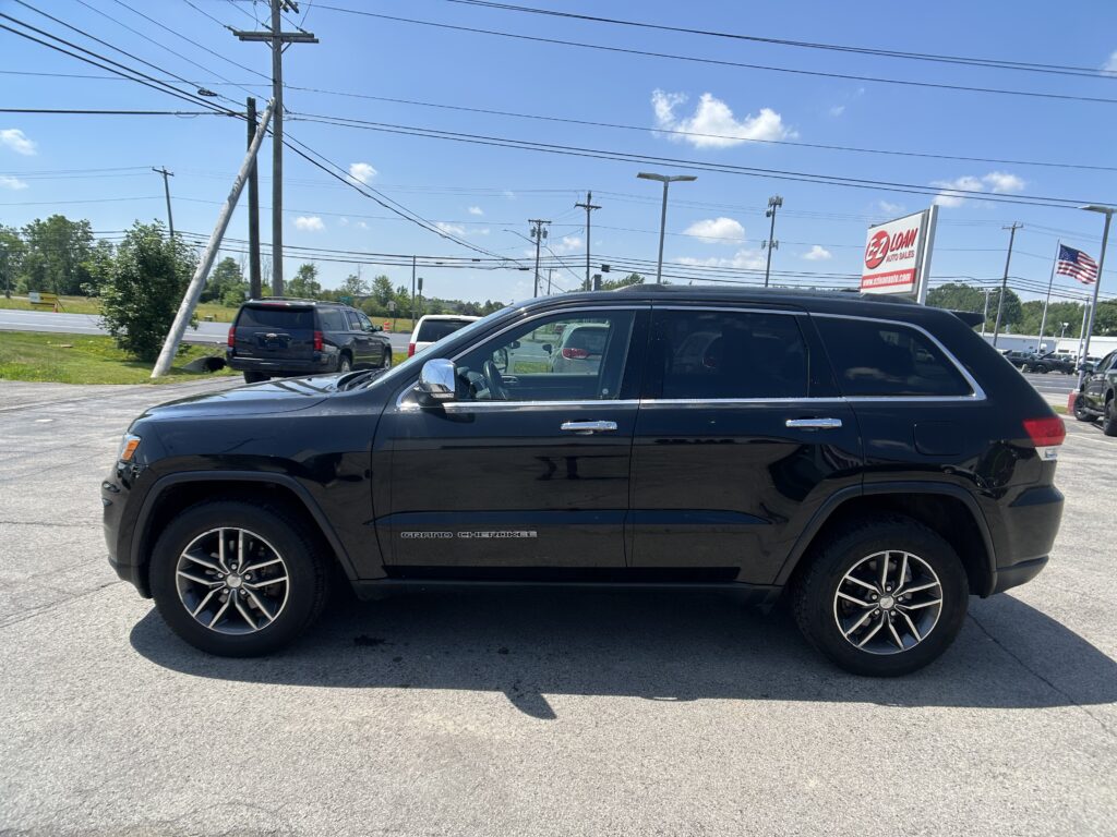 Black Jeep Grand Cherokee parked in a dealership lot with power lines overhead and an EZ LOAN Auto Sales sign in the background.