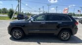 Black Jeep Grand Cherokee parked in a dealership lot with power lines overhead and an EZ LOAN Auto Sales sign in the background.