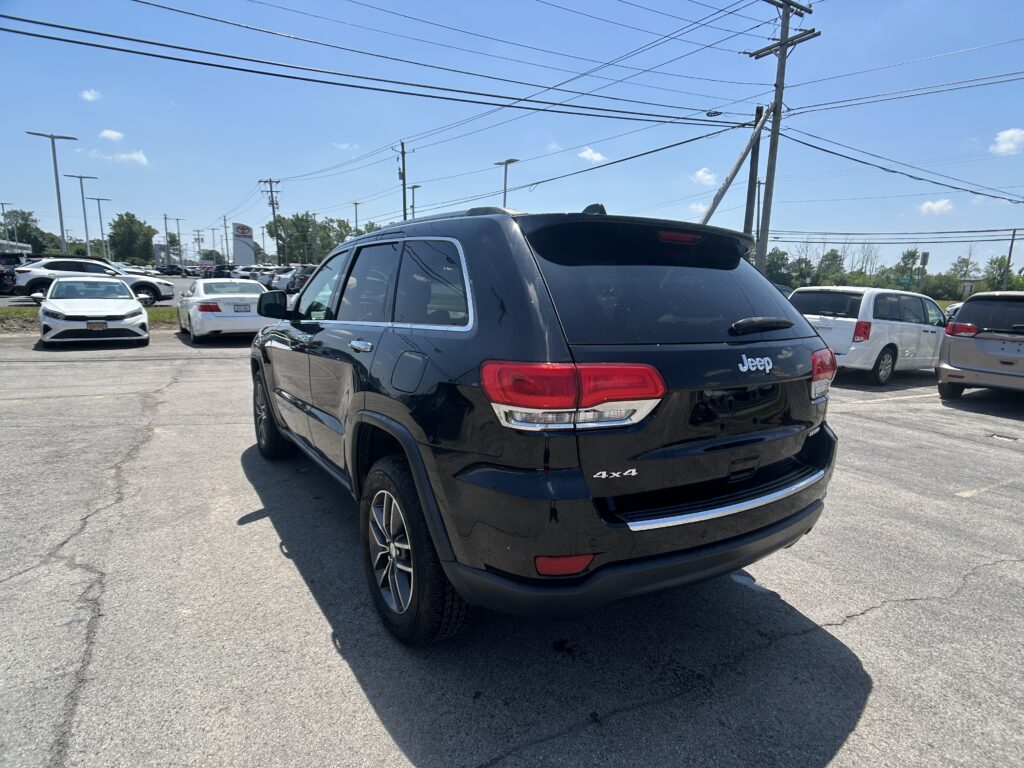 Black Jeep SUV in the foreground, rear three-quarter view, in a crowded parking lot under power lines.