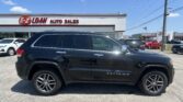 Black Jeep Grand Cherokee parked in a car dealership lot with the E-Z Loan Auto Sales sign visible on the building behind it.