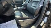 Interior of a car with black leather front seats, center console, and steering wheel on the left side, door open.