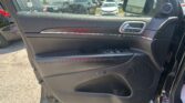 Inside of a car door panel with window control buttons and chrome handle, view of a parking lot outside the window.