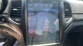 Car infotainment touchscreen showing rearview camera view with parking lines and app icons above the display.