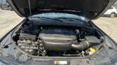 Open hood of a black SUV exposing the engine bay and battery components in daytime parking lot.