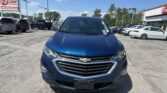 Front view of a blue Chevrolet SUV in a car dealership lot with other vehicles and an EZ LOAN sign in the background, under a blue sky.
