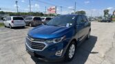 Blue Chevrolet SUV in foreground at a car dealership lot, with minivans behind and an EZ Loan sign in the background.