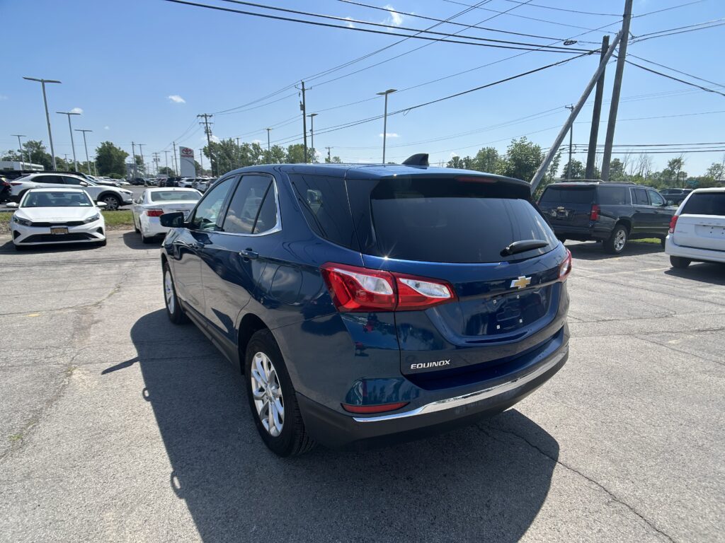 Blue Chevrolet Equinox in the foreground of a crowded car dealership lot on a sunny day, with other cars and power lines in the background.