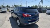 Blue Chevrolet Equinox in the foreground of a crowded car dealership lot on a sunny day, with other cars and power lines in the background.