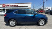 Blue SUV (Equinox) in foreground at an auto dealership with 'E-Z LOAN AUTO SALES' sign on white building and other vehicles nearby under a clear blue sky