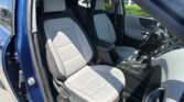 Open-car-door interior: two front gray seats with quilted pattern and center console, driver-side view in a blue vehicle.