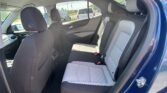 Interior of a blue car showing the back seat with light gray quilted upholstery and black seat belts; parking lot visible through windows.