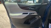 Interior of a car door showing the armrest, window controls, and chrome handle with the side mirror visible; outside is a dealership parking lot with many vehicles.
