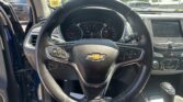 Inside a car cockpit: steering wheel with Chevrolet emblem, instrument cluster, and center touchscreen visible in daylight outside the windshield