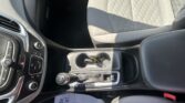 Interior of a car showing the driver and front passenger area: center console with cup holders, gear shifter, and climate controls visible; a paper on the footwell partially shows printed text.
